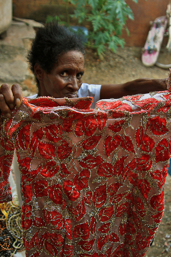 The victim's mother holds up the red-beaded dress he wore during samba performances in Carnival [Priscilla Moraes/Al Jazeera] 