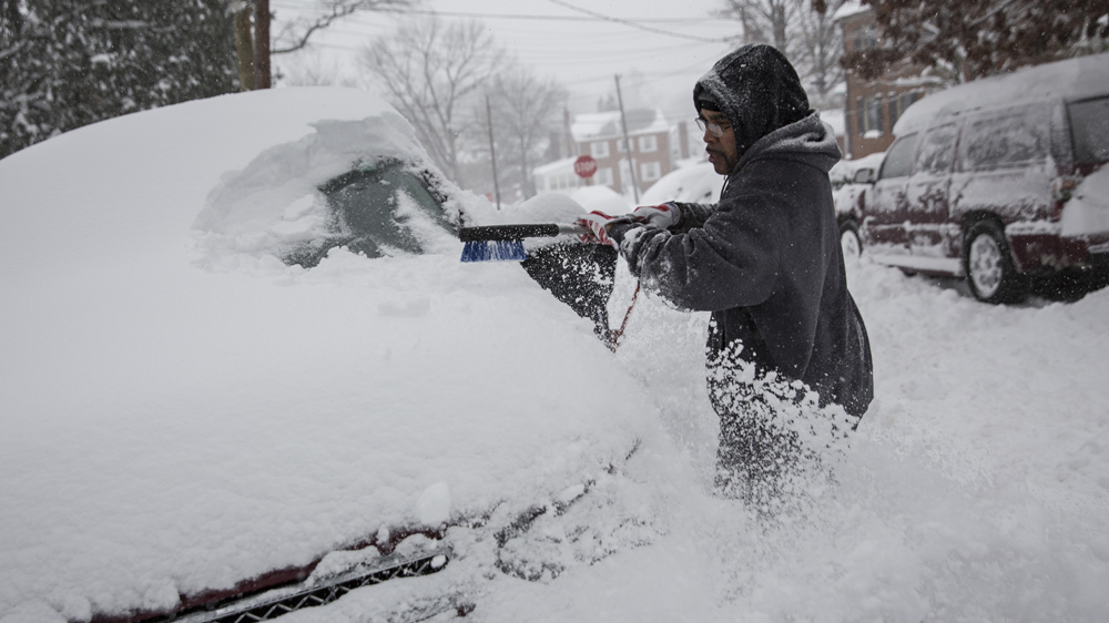 A man clears snow from his car in Washington DC on Saturday [Drew Angerer/EPA] 