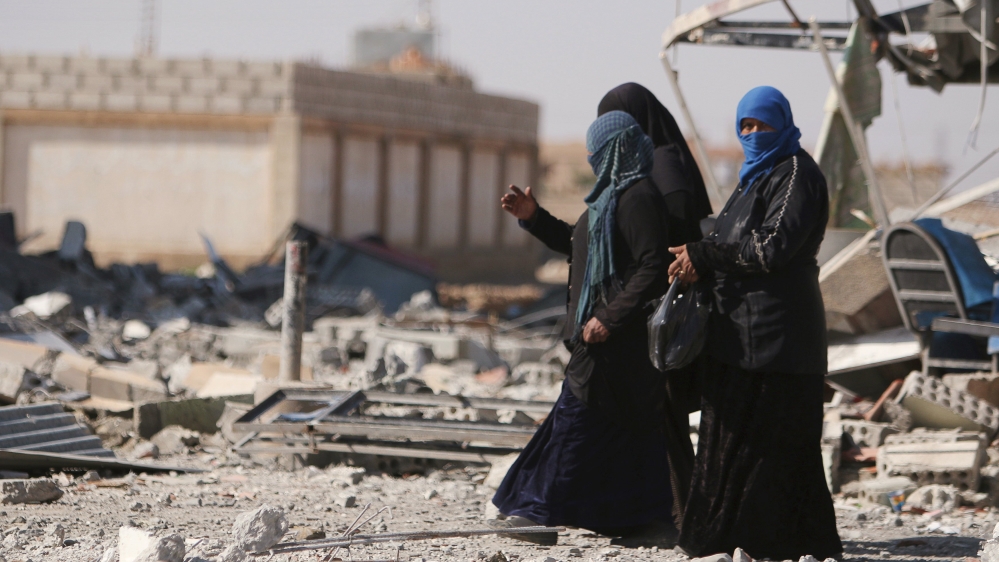 Women walk on rubble in al-Shadadi town, in Hasaka province