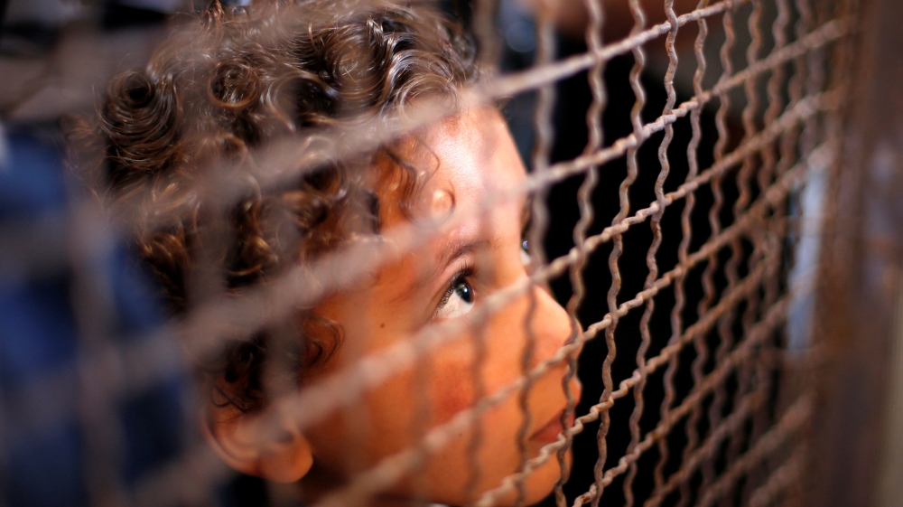 Boy looks through a fence as he waits with his family for a travel permit
