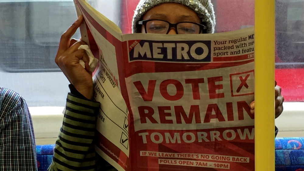 A woman reads a newspaper on the underground in London with a ''vote remain'' advert for the BREXIT referendum
