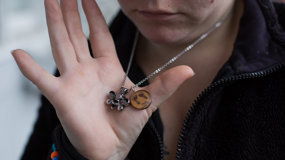  Tiffany shows the necklace that reminds her of her late daughter. The bee holds her daughter's ashes, while the other charm has small designs of her daughter's footprints [Carolyn Bick/Al Jazeera] 