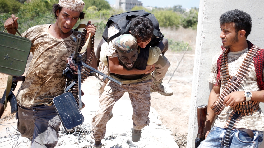 A fighter of Libyan forces allied with the U.N.-backed government runs for cover with another fighter while carrying a wounded fighter during a battle with Islamic State fighters in Sirte