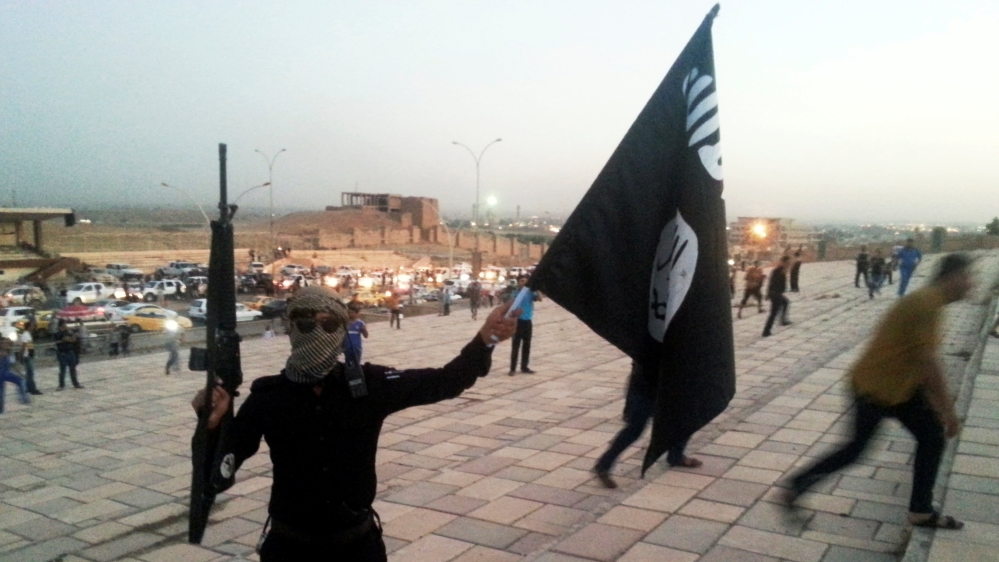 A fighter of the ISIL holds a flag and a weapon on a street in Mosul