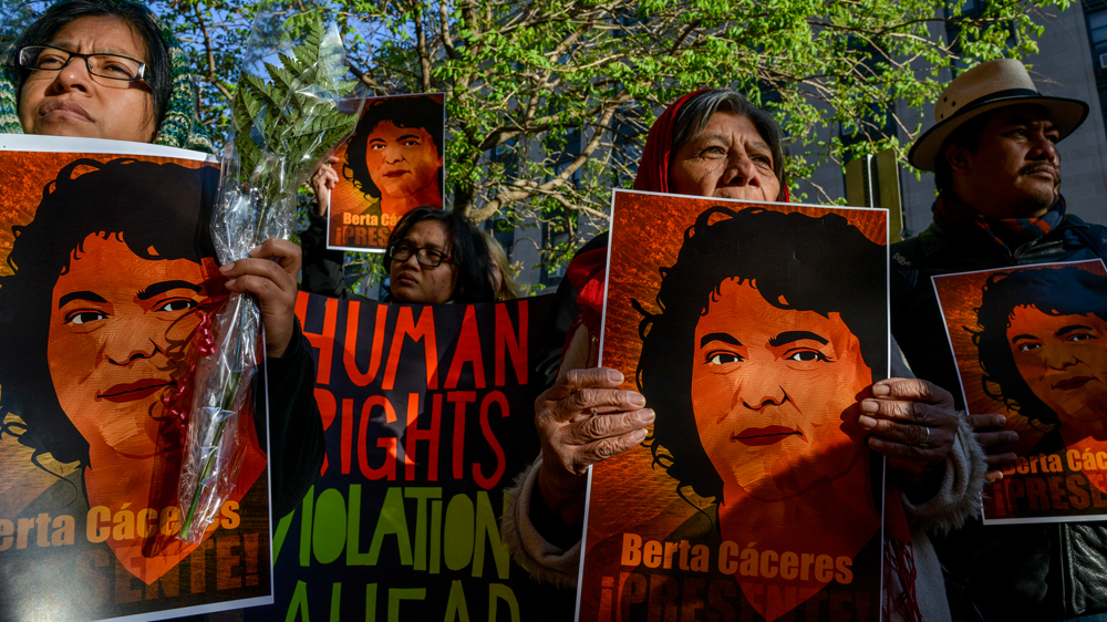 Demonstrators hold signs with Berta Caceres's photo and banners denouncing human rights violations.