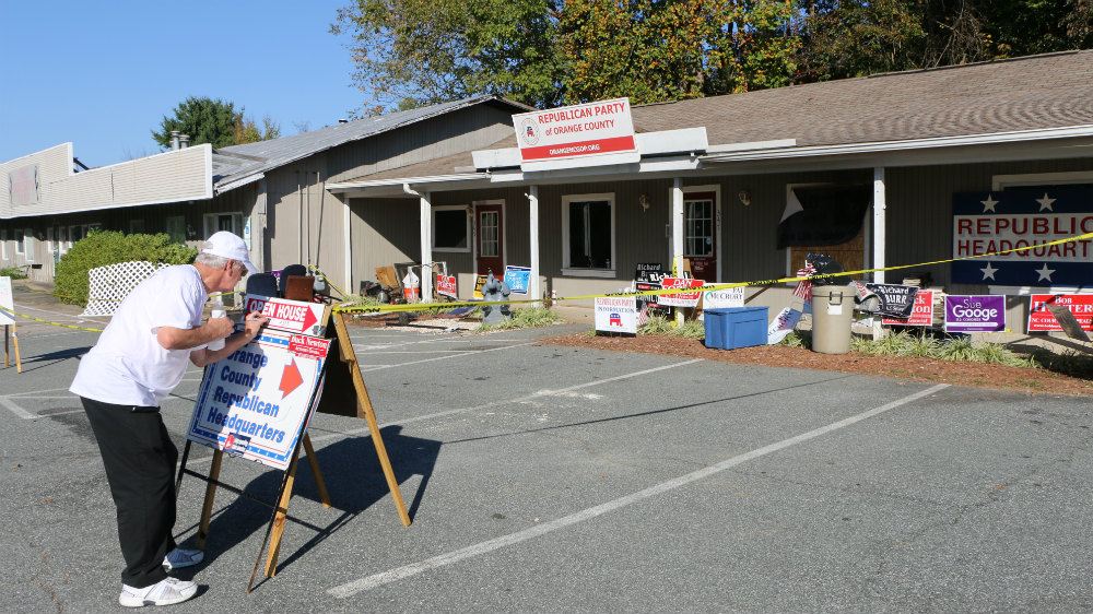 Daniel Ashley puts up a sign to the new Republican headquarters after the party's offices were firebombed [Julienne Gage/Al Jazeera]