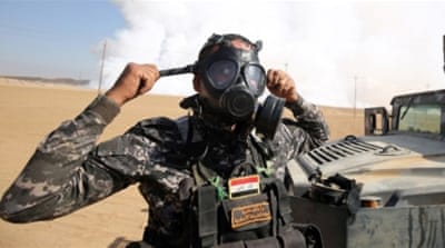Iraqi forces wear gas masks for protection as smoke billows in the background after ISIL fighters torched a factory in Mosul [AFP]