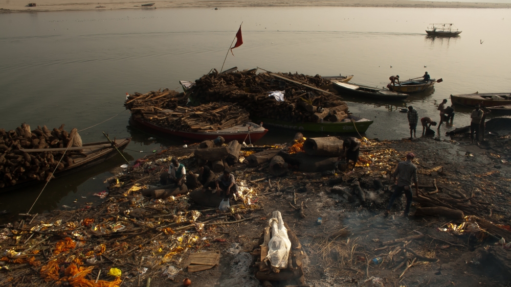 A corpse wrapped in white cotton lies on a funeral pyre at Manikarnika. In Hinduism, the dead are cremated. Hindus believe that fire is a natural element that cleanses the soul and liberates it from the body. [Radhika Iyengar/Al Jazeera]