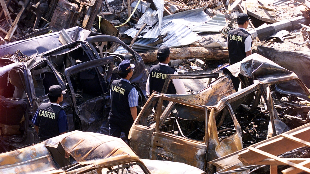 Indonesian forensic policemen walk past destroyed cars near the site of 2002 bomb blasts at Kuta on Indonesia’s resort island of Bali