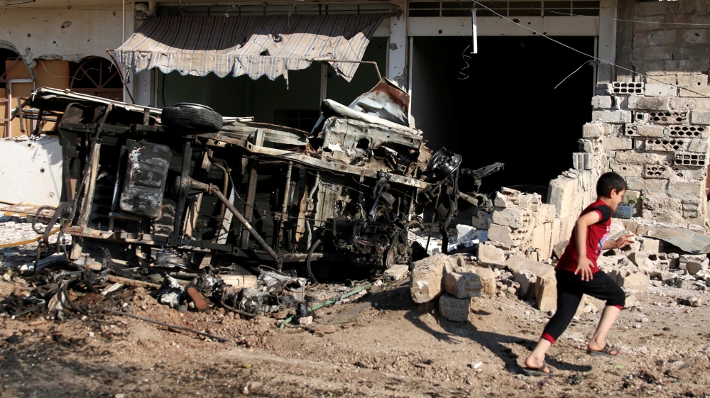 A boy walks past a damaged vehicle at a site hit by an airstrike in the rebel-held Tafas town