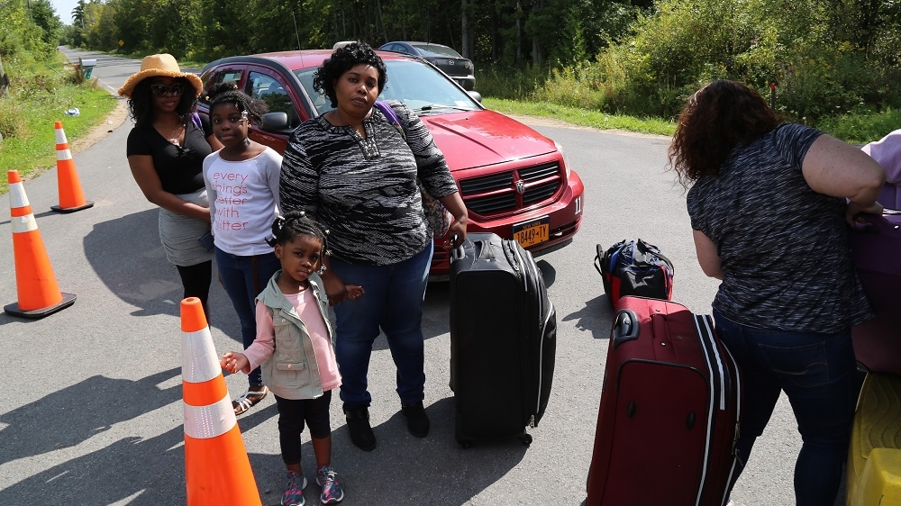 Chelsie David, centre with suitcase, waits with her family for their luggage to be unloaded from a taxi before crossing the border at Roxham Road.