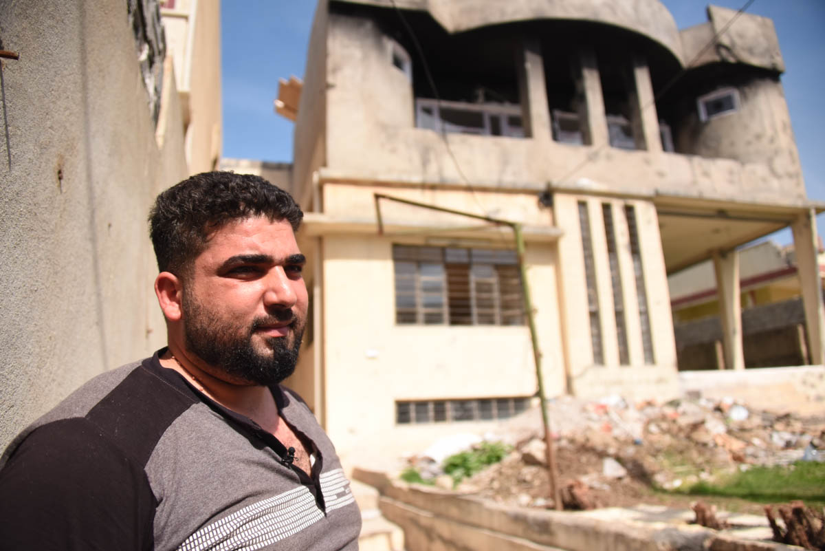 Photo 18 A man stands in front of his rented house. Alaa, a father of three children, lives in a rented house in Mosul with two other families. They are twelve people in all crammed in one home. “Most
