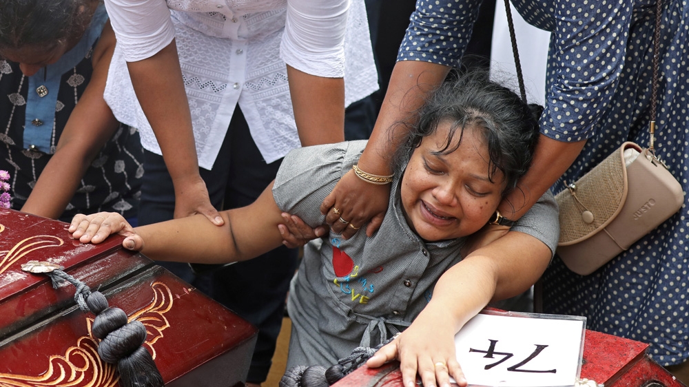 A woman mourns next to two coffins during a mass burial at a cemetery near St. Sebastian's Church in Negombo [Athit Perawongmetha/Reuters]
