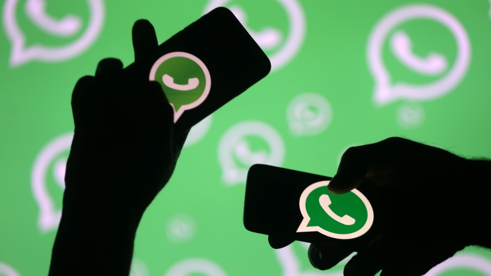 Men pose with smartphones in front of displayed Whatsapp logo in this illustration