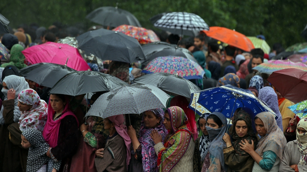 Women stand under umbrellas as they watch the body of Zakir Rashid Bhat