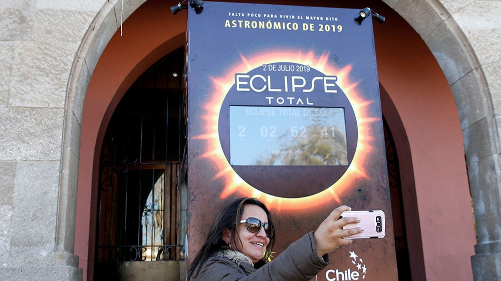 A woman takes a photo of a digital clock behind her, which shows the time left till the total solar eclipse, in Coquimbo, Chile