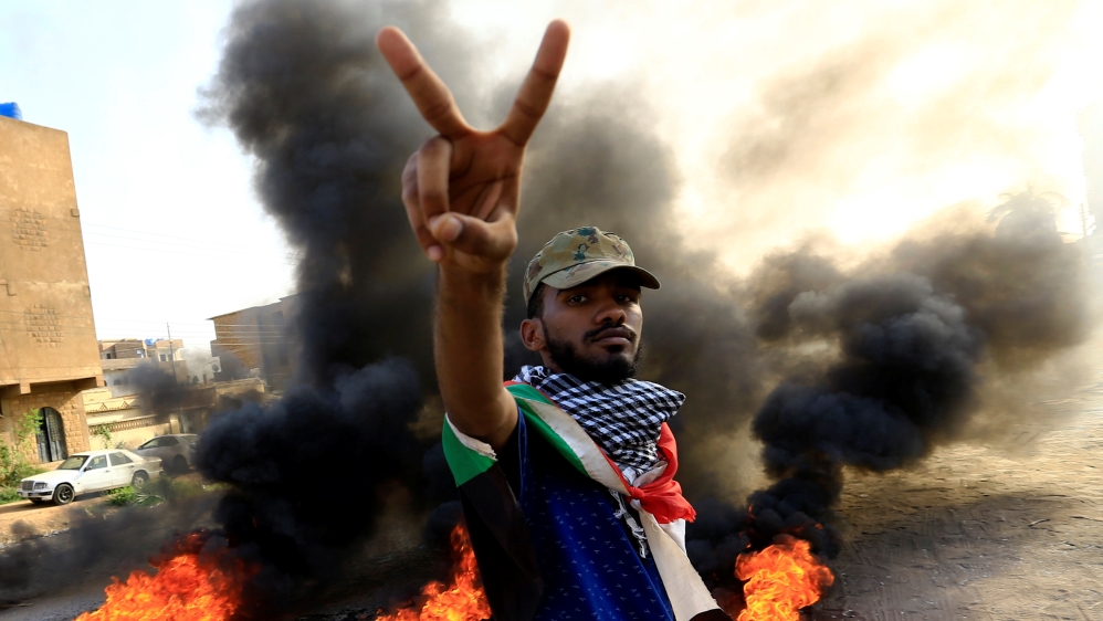 A protester gestures as he burns tyres during a demonstration against a report of the Attorney-General on the dissolution of the sit-in protest in Khartoum