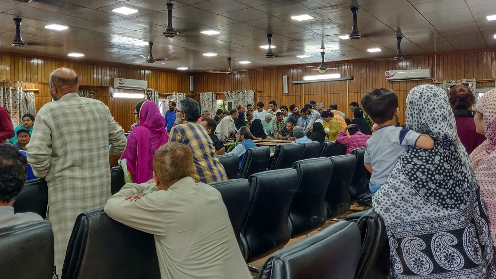 Kashmiris crowd around an official to use a phone at a government office