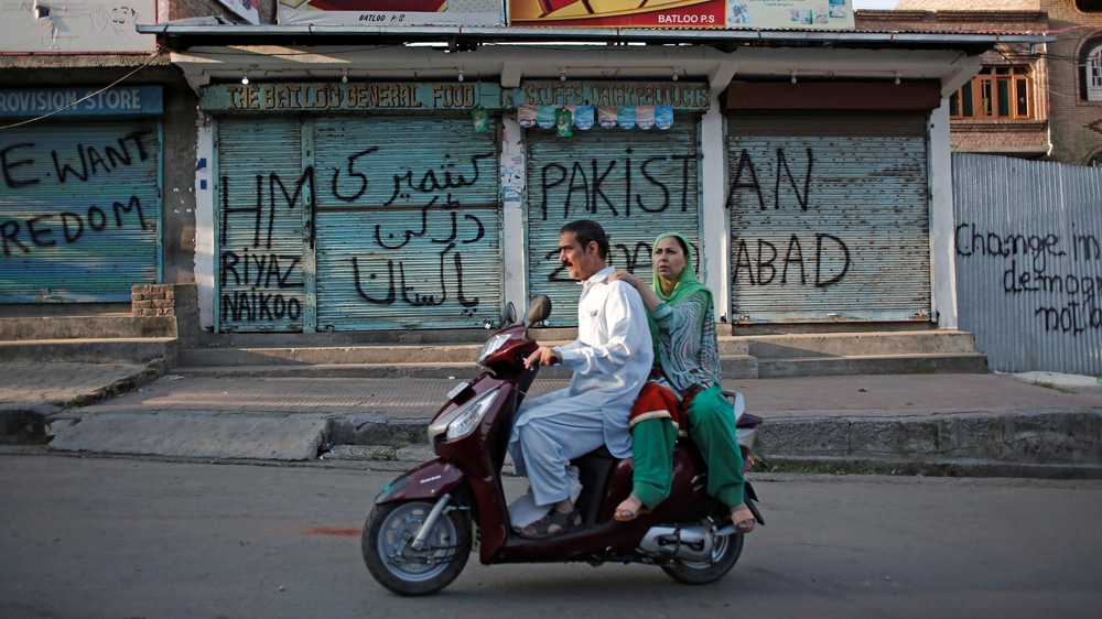 Kashmiris ride on a scooter past the closed shops painted with graffiti during restrictions in Srinagar