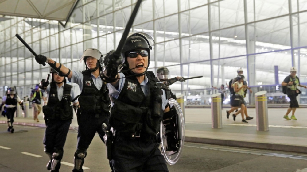 Policemen with batons and shields shout at protesters during a demonstration at the airport in Hong Kong