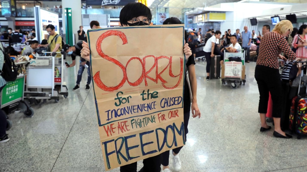 A protester displays a placard to stranded travellers during a demonstration at the airport on August 13
