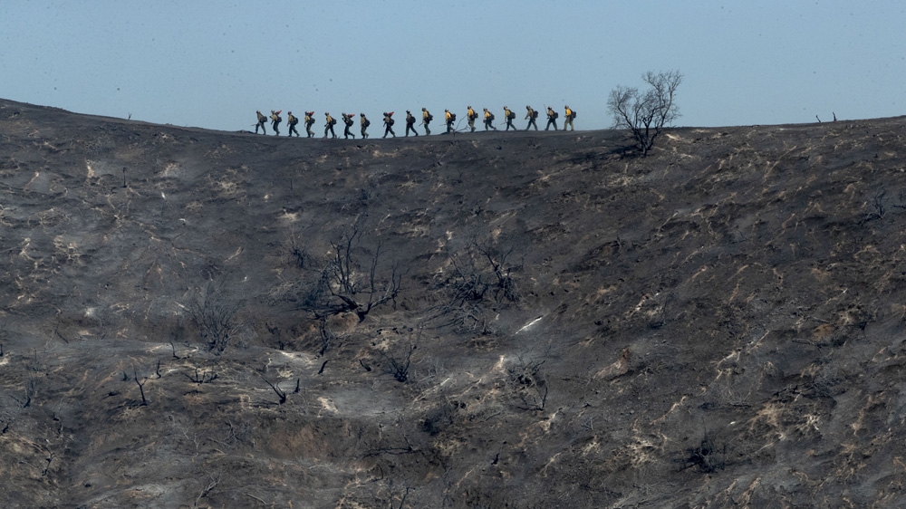 Fire crews walk along a blackened ridge as they battle the Getty fire in Los Angles