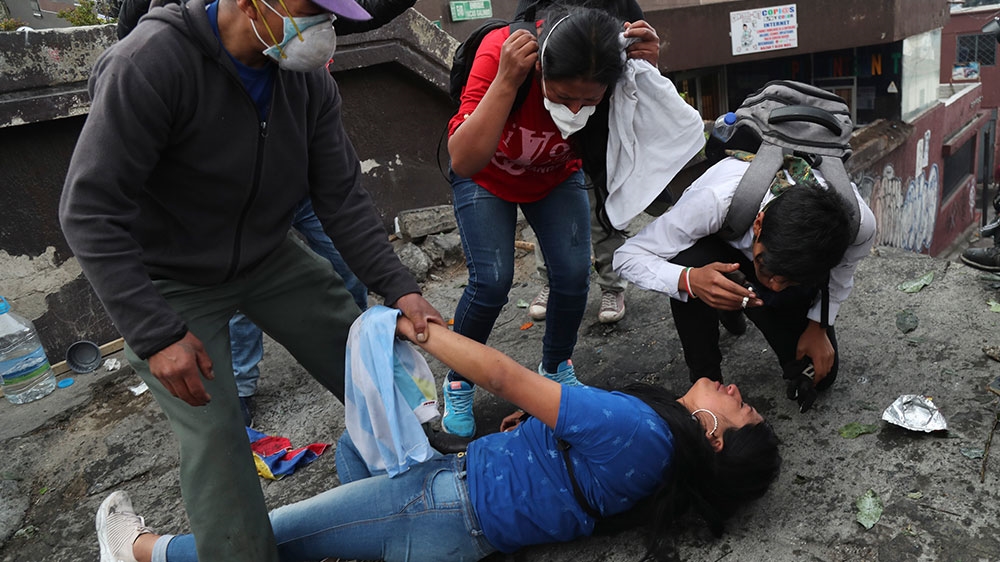 People come to the aid of a woman affected by tear gas launched by security forces to disperse anti-government protesters from the vicinity of the National Assembly, in Quito, Ecuador