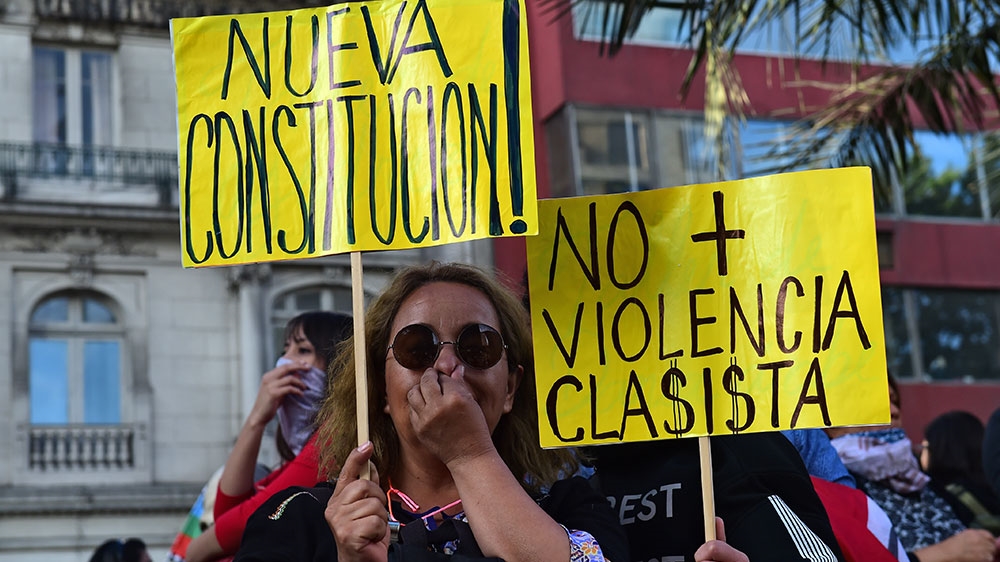 People hold signs reading ‘New constitution!’ and ‘No more classist violence’ as they protect themselves from tear gas while taking part in a protest in Santiago earlier this month