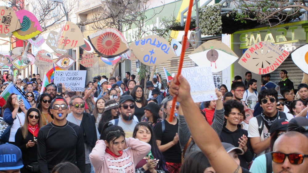 Protesters in Antofagasta march Monday evening under a protest art installation calling attention to severe eye injuries during the crisis