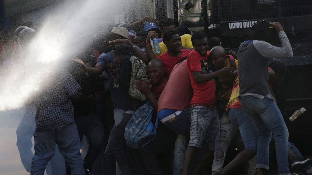 Protesters take cover behind a Haitian National Police anti-riot truck during clashes at a demonstration to demand the resignation of Haitian president Jovenel Moise, in the streets of Petion Ville, Port-au-Prince