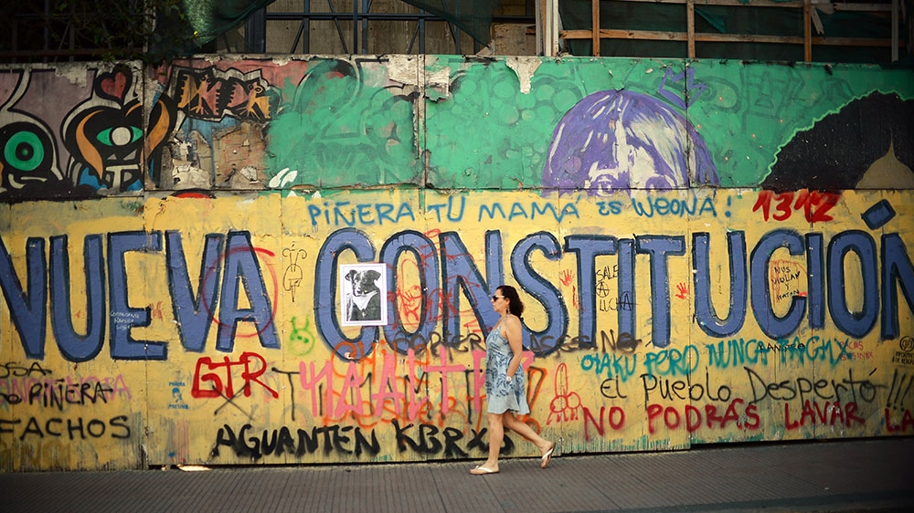 A woman passes by graffiti that reads ‘New Constitution’ in Santiago
