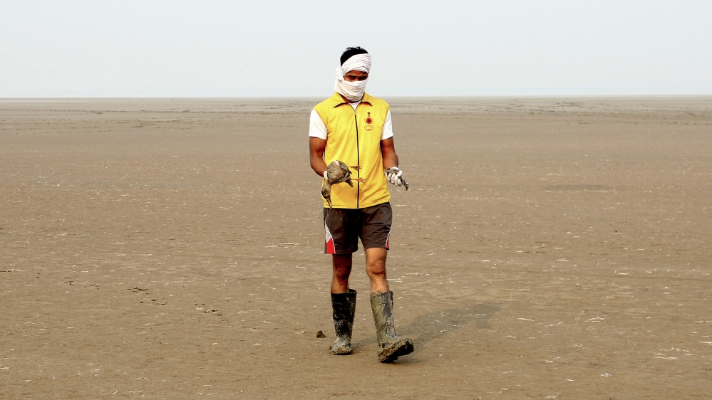 In this photo taken on November 16, 2019, a worker walks as he holds dying birds in his hands at Sambhar Salt Lake in India's northern state of Rajasthan, where thousands of migratory birds were myste