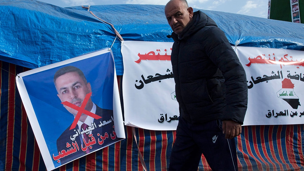 A protester walks past a poster with a defaced picture of the governor of the southern Basra province, Asaad al-Eidani, and Arabic words that mean ‘rejected by the people’, during the continuing protests, in Tahrir square, in Baghdad, Iraq