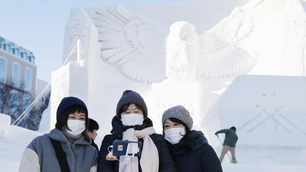 Visitors wearing masks amid concern over the spread of a new coronavirus take a selfie in front of a snow sculpture on the first day of the annual Sapporo Snow Festival in Hokkaido, northern Japan.