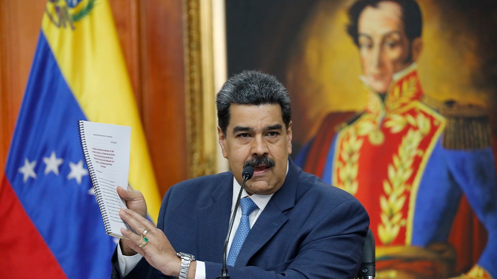 Venezuelan President Nicolas Maduro holds up a copy of his country’s case taken to the International Criminal Court regarding US sanctions during a news conference at Miraflores presidential palace in Caracas, Venezuela