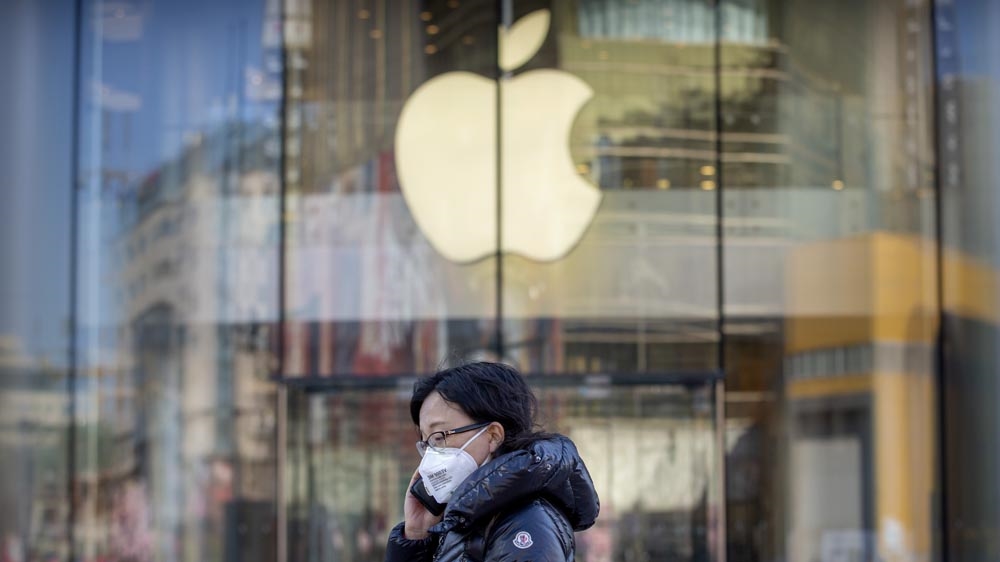 A woman wears a face mask as she walks past an Apple store that is temporarily closed due to health concerns in Beijing.