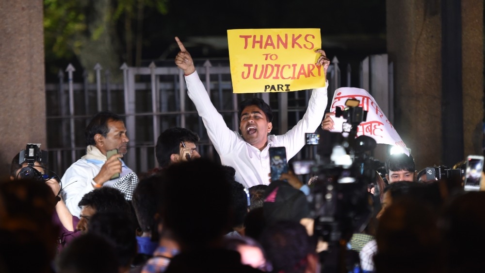 An indian man holds a placard outside the gates of Tihar Jail after the execution of four men convicted in the gang rape and murder of a student in 2012