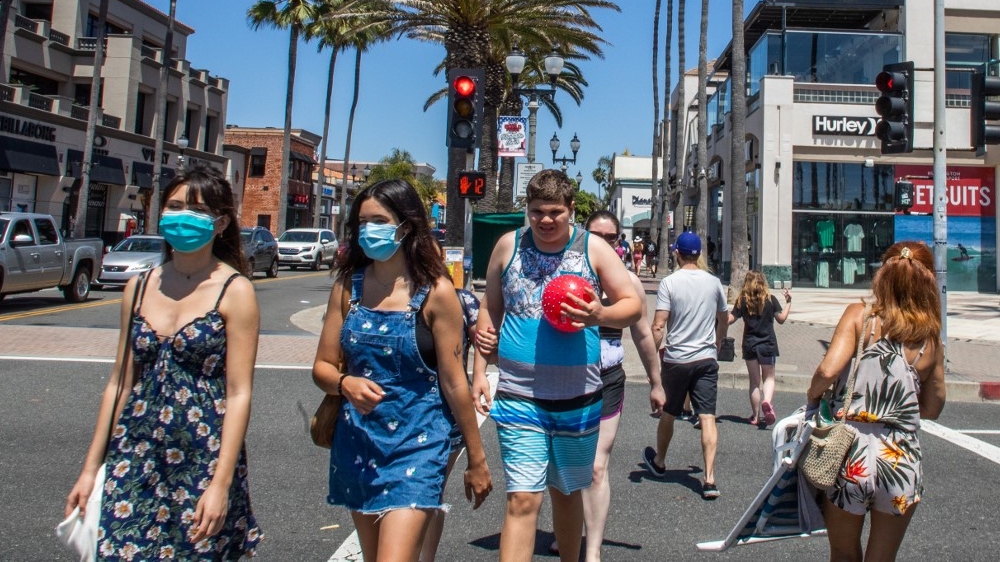 People cross the street, some wearing masks, amid the coronavirus pandemic in Huntington Beach, California.