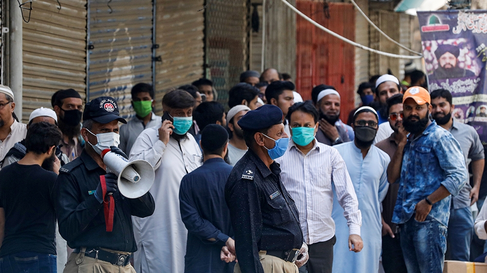 A police officer uses a megaphone to disperse shopkeepers gathered to reopen their shops at a closed market in Karachi