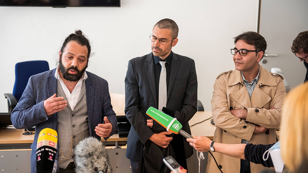 Attorney Patrick Kroker (C) and co-plaintiffs Wassim Mukdad (L) and Hussein Ghrer (R) answer journalists’ questions outside the courtroom during a break in the trial