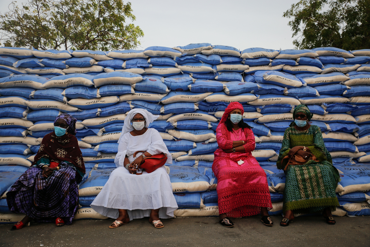 Women sit on sacks of rice during an aid distribution to families in need headed by the Mayor of Dakar on April 10, 2020. In March, President Macky Sall announced economic measures to mitigate the cor