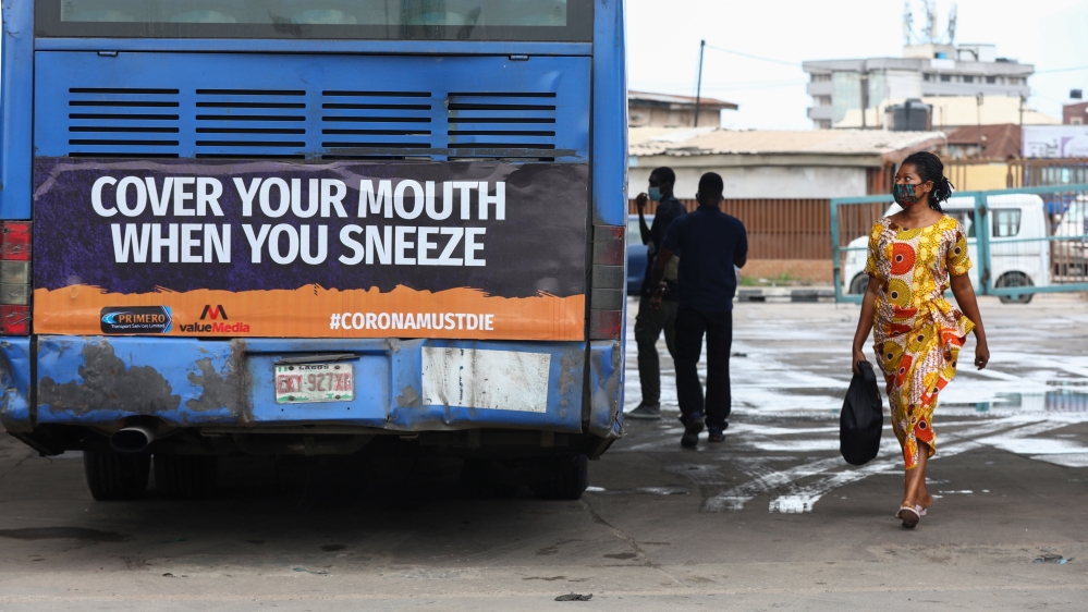A woman wearing a protective face mask walks past a public bus in Lagos, the epicentre of the crisis in Nigeria
