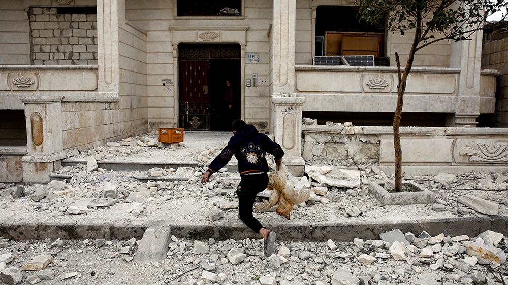A Syrian boy removes a dead chicken from the debris of a building hit in an air raid in Idlib