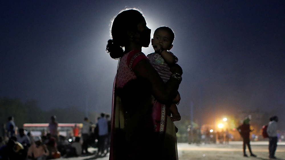 A woman and her baby wait for a bus to take them to a railway station to board a train to their home state of Uttar Pradesh, after a limited reopening of India’s giant rail network