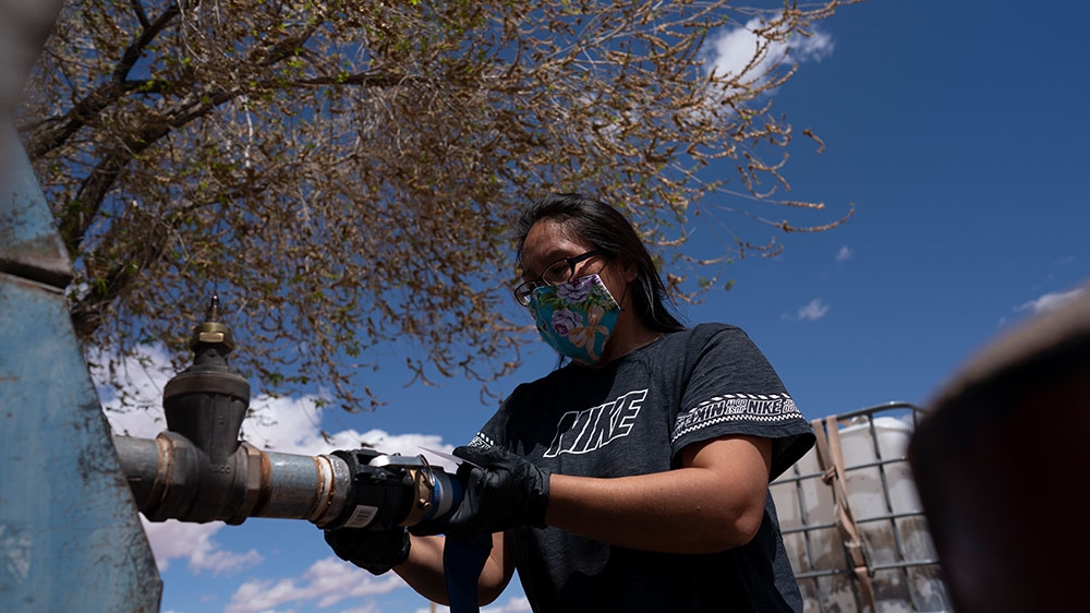 Raynelle Hoskie attaches a hose to a water pump to fill tanks in her truck outside a tribal office on the Navajo reservation in Tuba City, Arizona