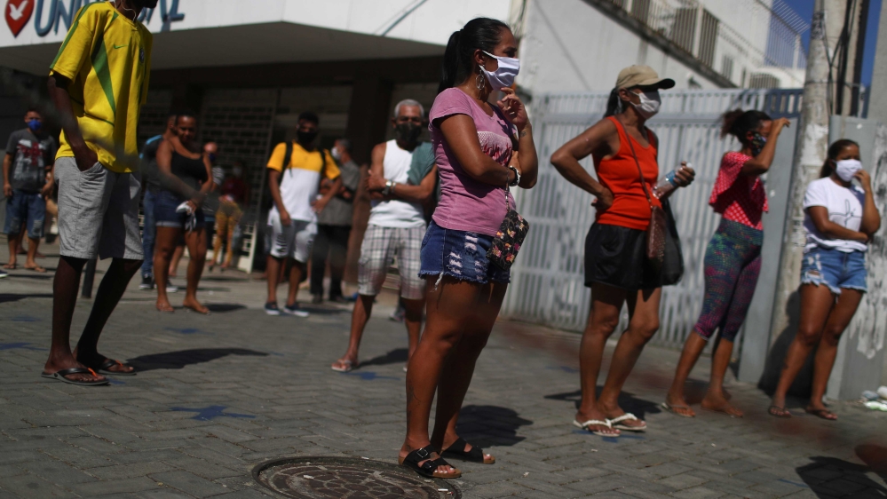 People wearing face masks standing on the marks for social distancing outside the Caixa public bank, as they wait to receive emergency aid given by the federal government in Rio de Janeiro, Brazil