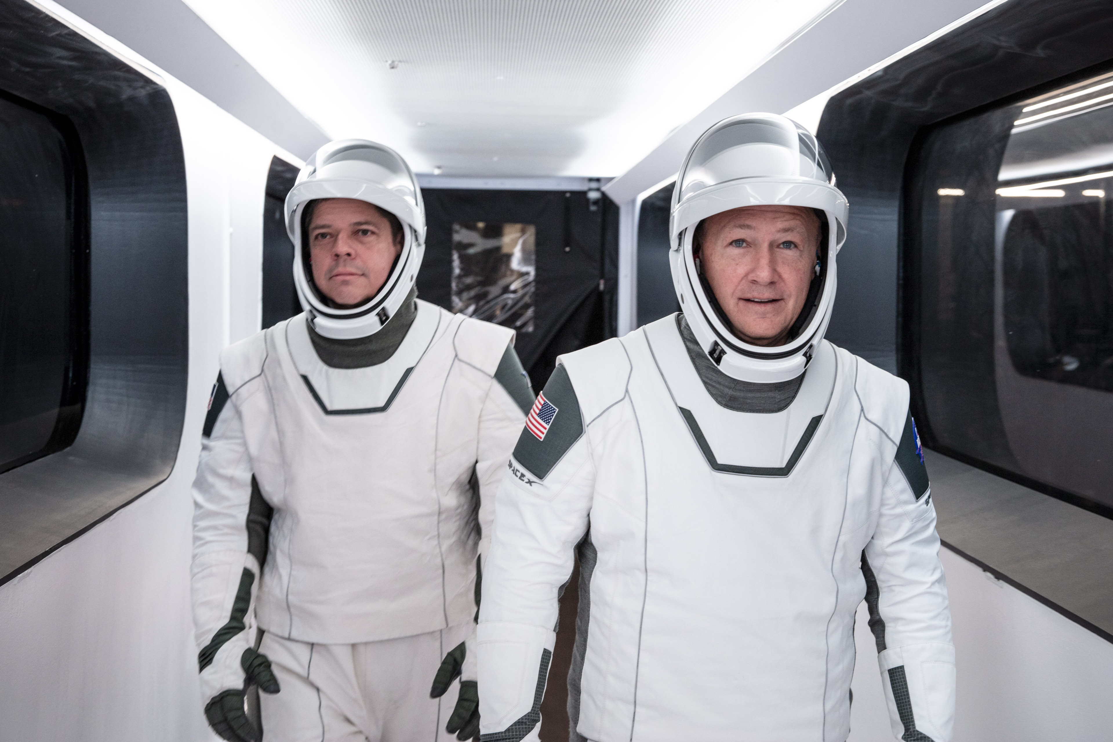 NASA astronauts Bob Behnken, left, and Doug Hurley, right, wearing SpaceX spacesuits, walk through the crew access arm connecting the launch tower to the SpaceX Crew Dragon spacecraft during a dress rehearsal at NASA’s Kennedy Space Center in Florida, the United States