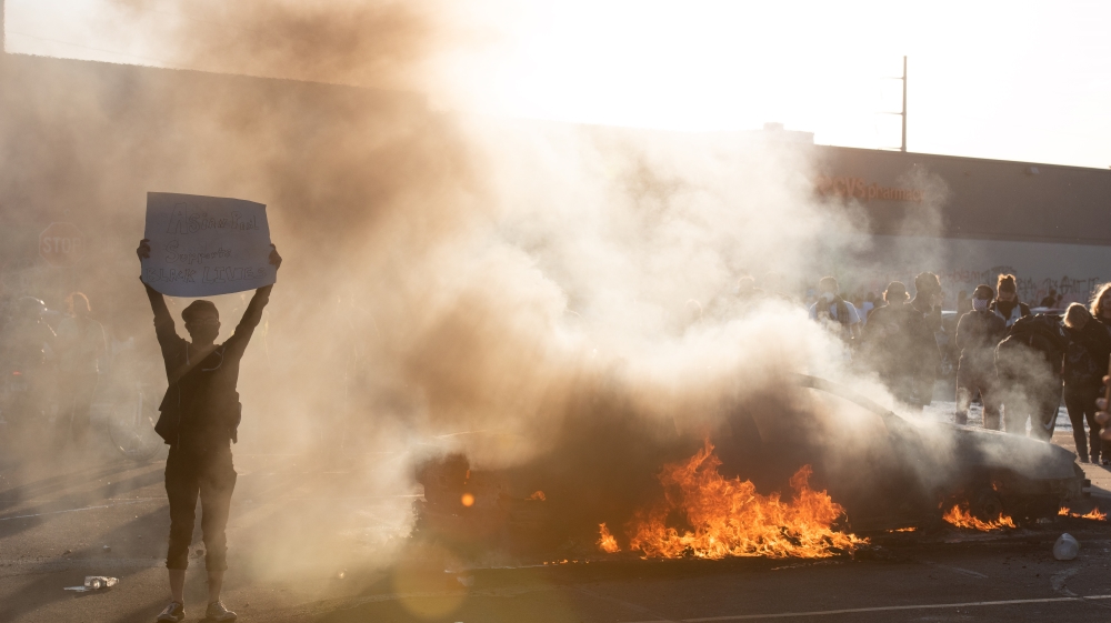 A protestor stands next to a burning car and holds a sign in support of the Black Lives Matter movement during the third day of protests over the death of George Floyd [Anadolu]