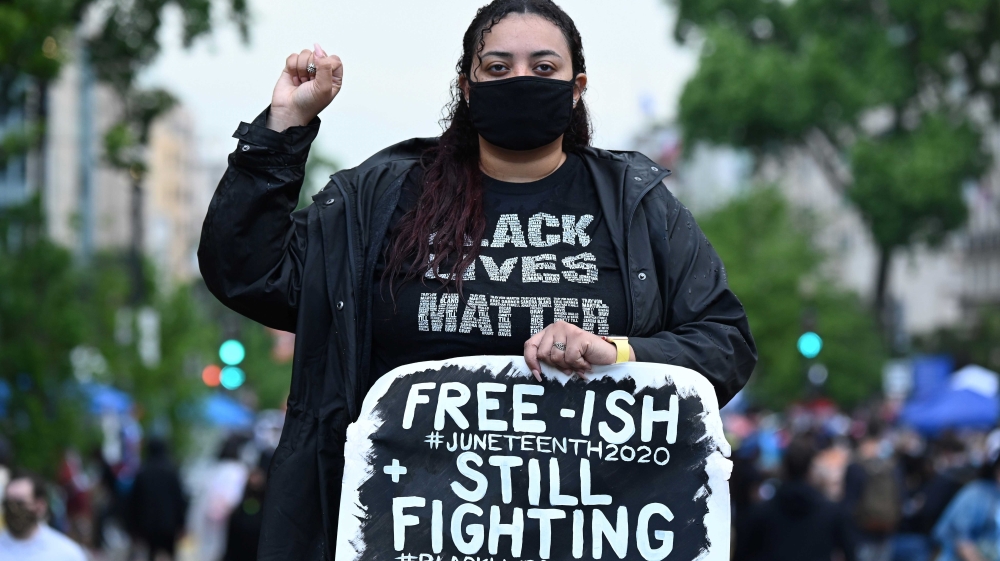 Aneisha Felton raising her fist while holding a sign during a protest to mark Juneteenth, near the White House, in Washington, DC