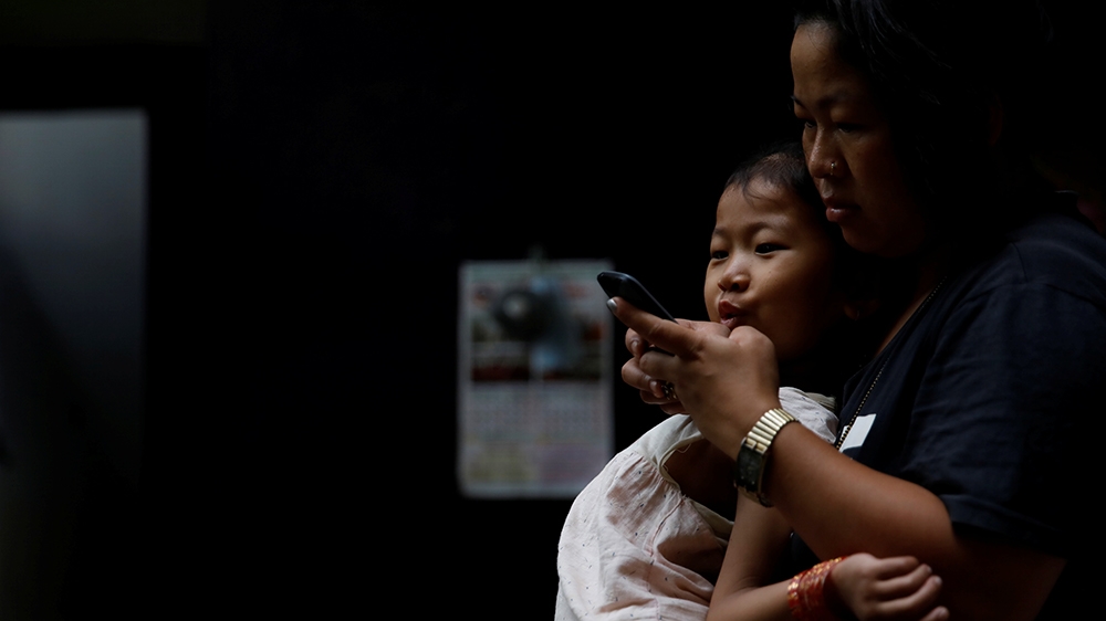 Limbu uses her mobile phone while her five-year-old daughter Masim sits on her lap, in Kathmandu